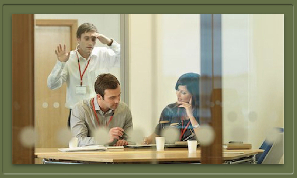 Man peers through office window at coworkers.