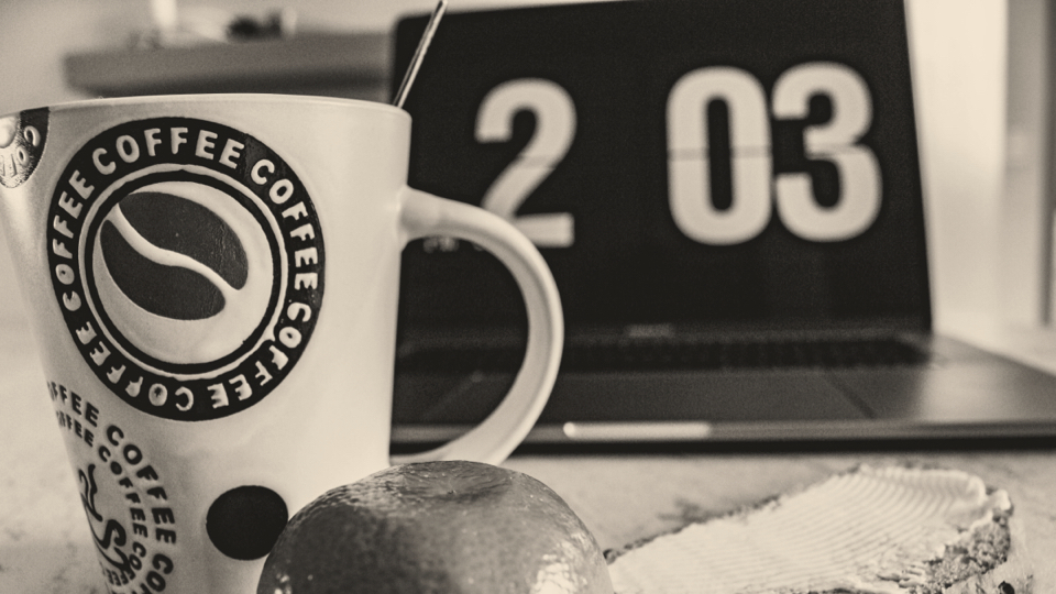 Coffee mug, toasted bread, orange, clock and a laptop